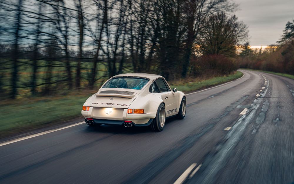 Cream Coupé, a Porsche 911 (964) reimagined by Theon Design: rear three-quarter view driving through a bend on a country road