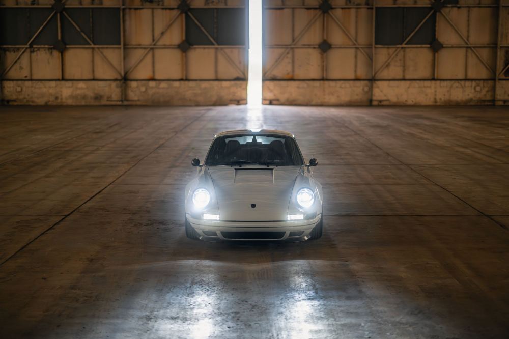 Silver Coupé, a Porsche 911 (964) reimagined by Theon Design: front view with headlights on in a hangar