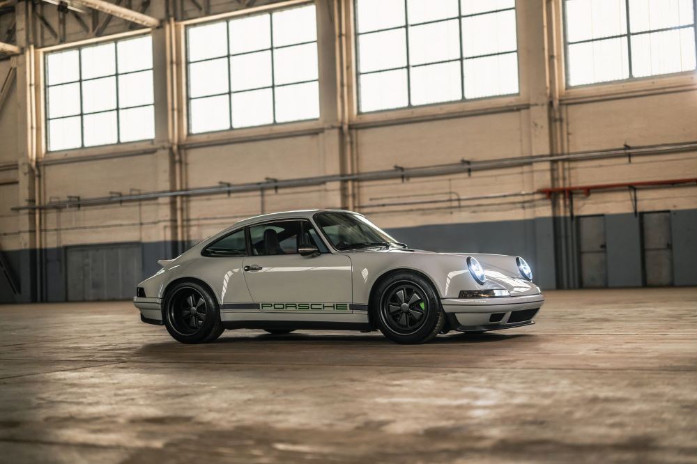 Silver Coupé, a Porsche 911 (964) reimagined by Theon Design: front three-quarter view with headlights on in a hangar