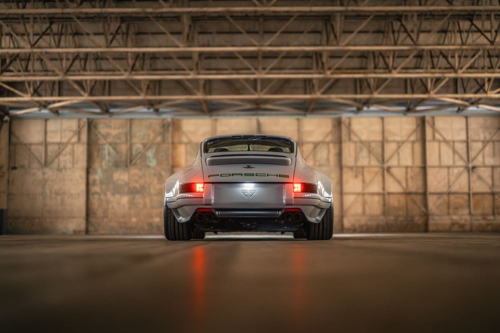 Silver Coupé, a Porsche 911 (964) reimagined by Theon Design: rear view with tail lights on in a hangar